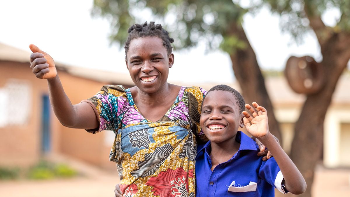 Eine Frau und ein Junge stehen eng beisammen, lachen und winken.