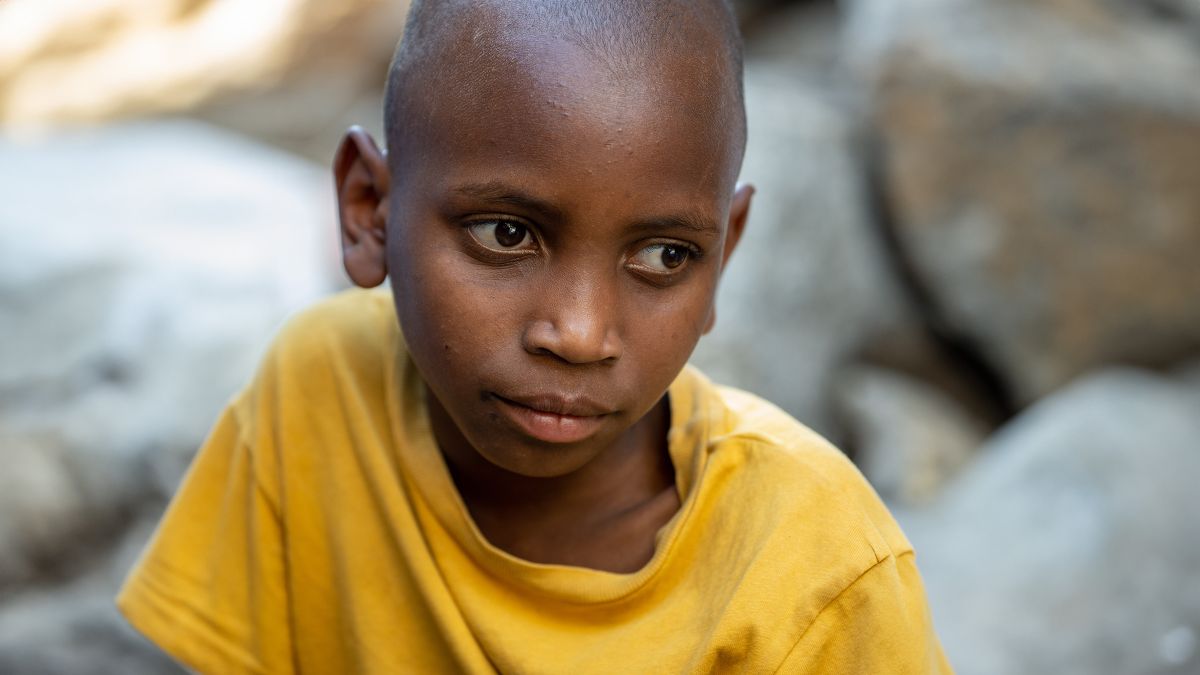 Ein etwa zehnjähriger Junge im gelben T-Shirt. Er sieht traurig aus.