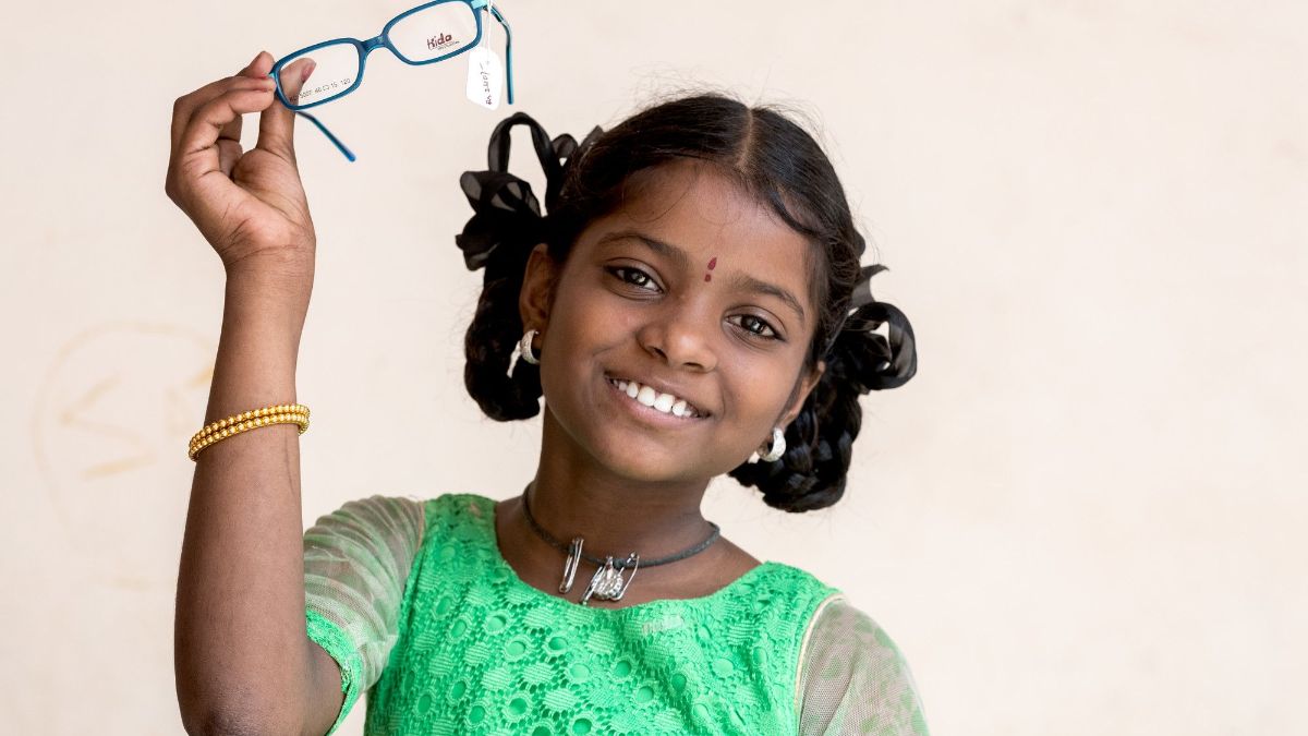 Ein Mädchen hält lachend eine Brille hoch.