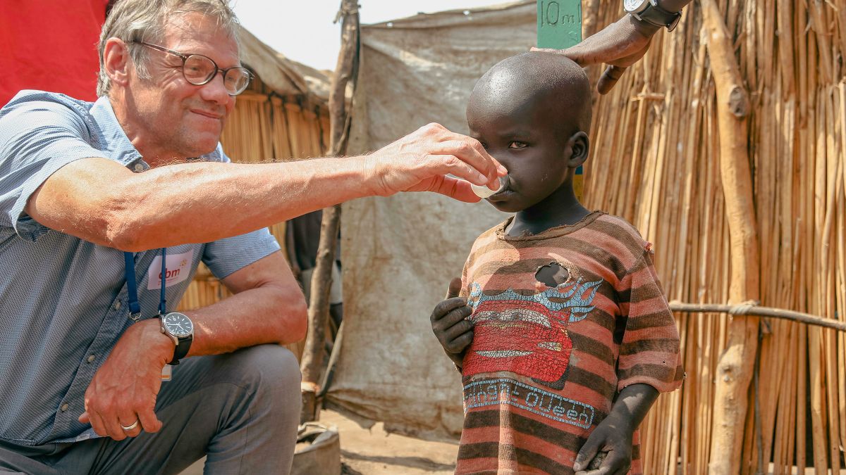 Ein Mann gibt einem Kind etwas aus einem Medikamentenbecher zu tringen.