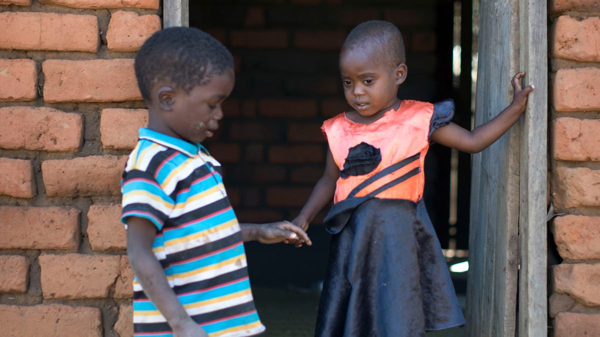 Eine junge Frau trägt ein etwa dreijähriges kleines Mädchen auf dem Rücken.