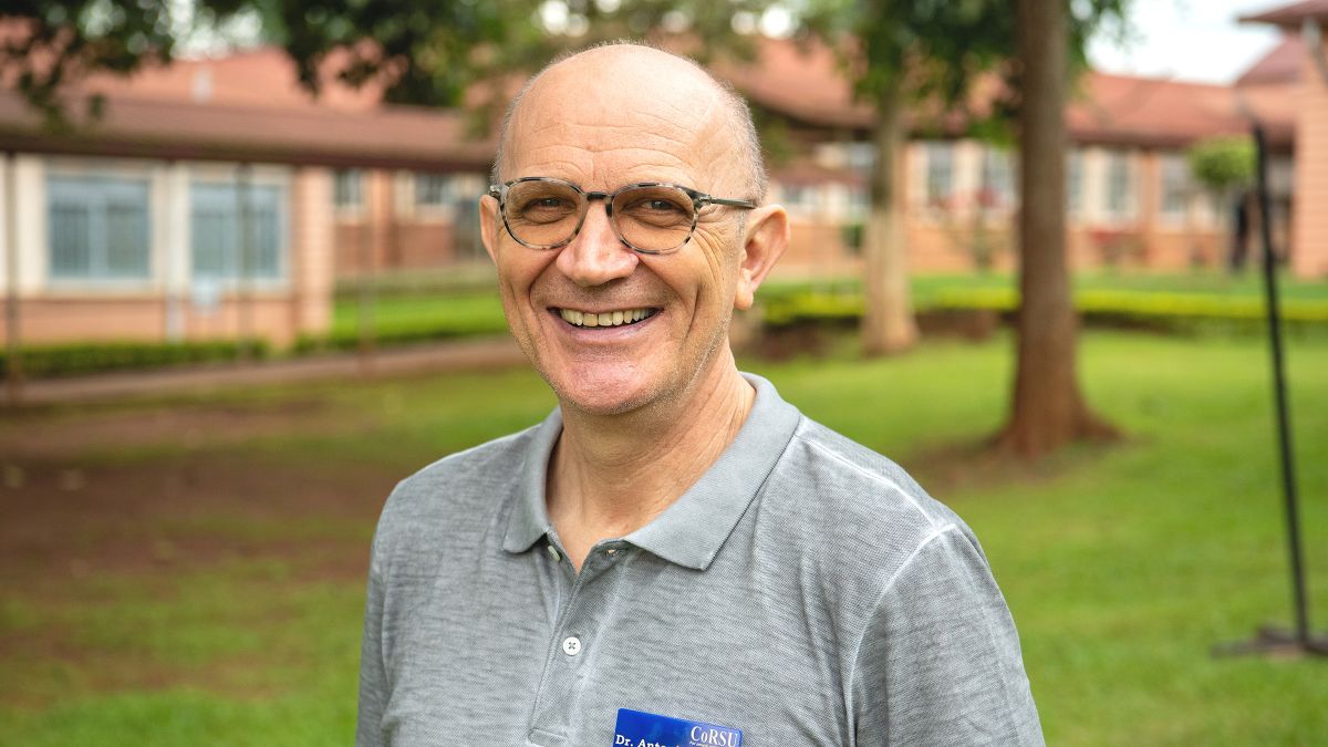 Ein Mann mittleren Alters steht vor einem geklinkerten Gebäude.