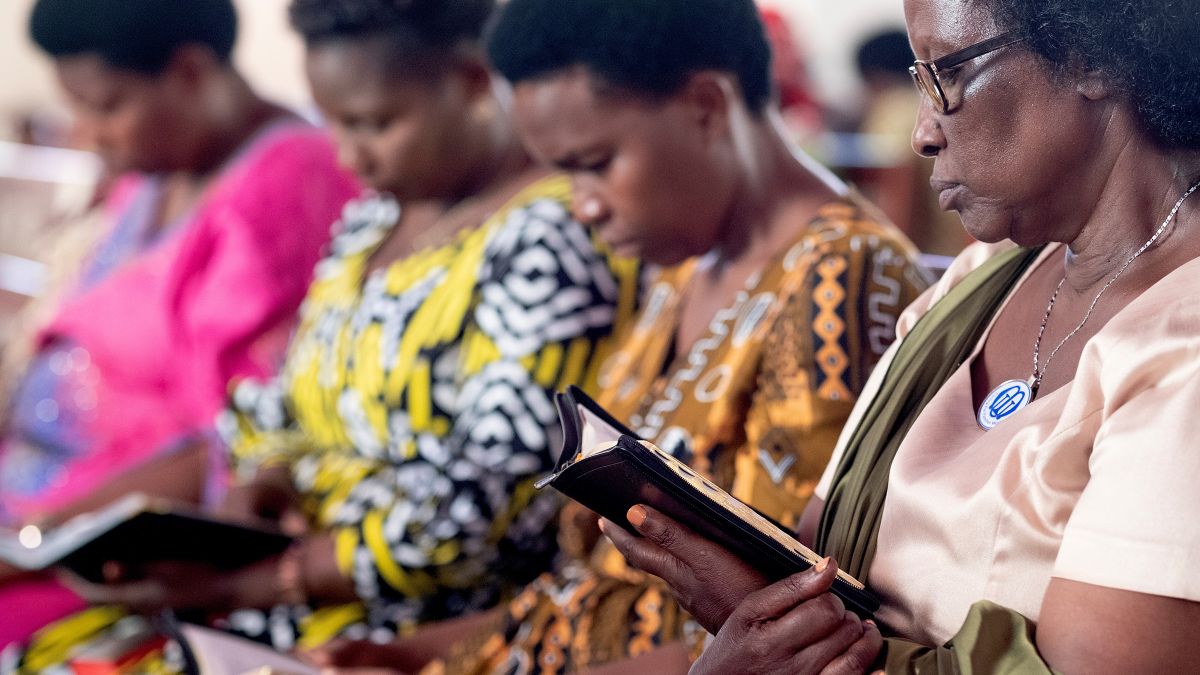 Frauen in bunten Baumwollkleidern sitzen in einer Reihe. Sie halten Bibeln in der Hand und lesen darin.