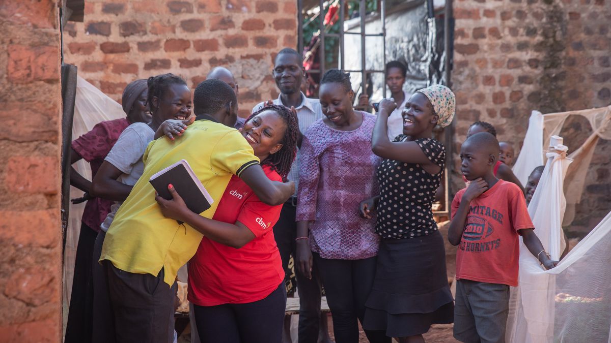 Eine Frau und ein Mann umarmen sich, weitere Frauen, Männer und Kinder stehen dabei. Die meisten lächeln.