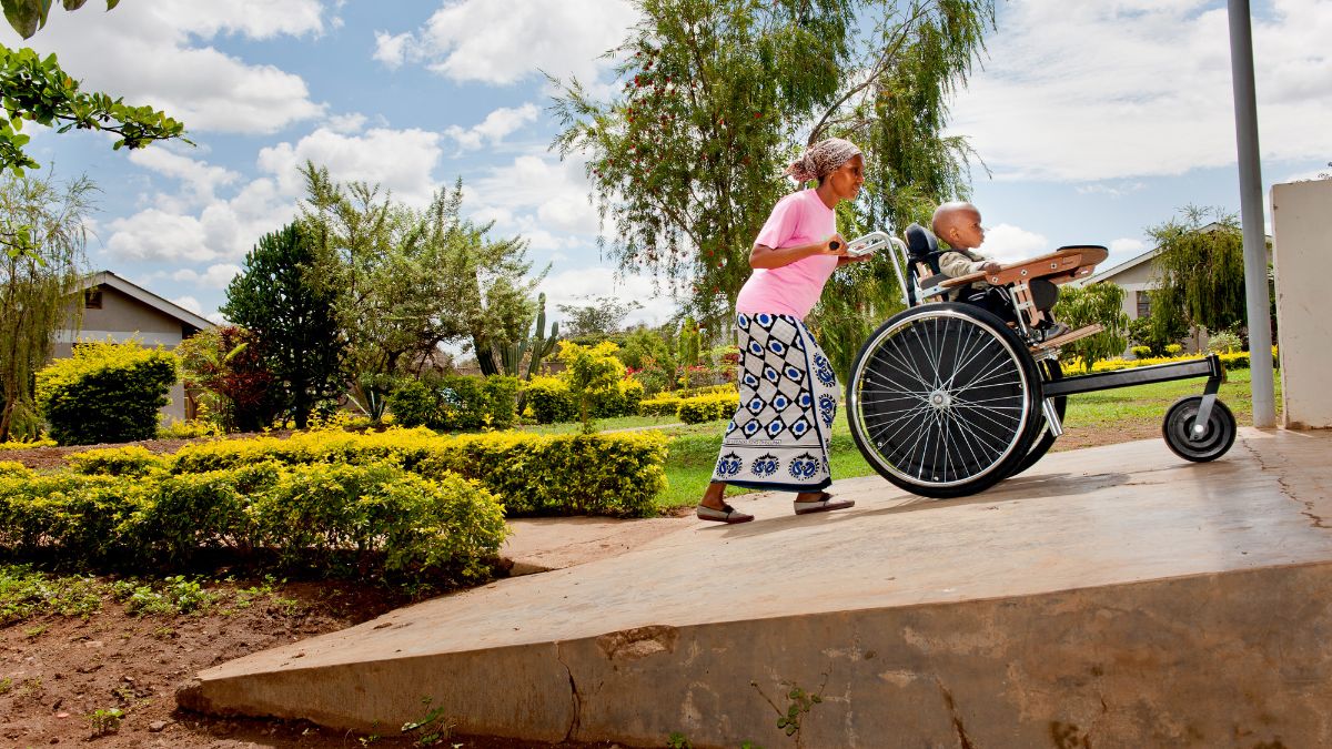 Eine afrikanische Frau schiebt ein Kind im Rollstuhl eine Rampe hinauf.