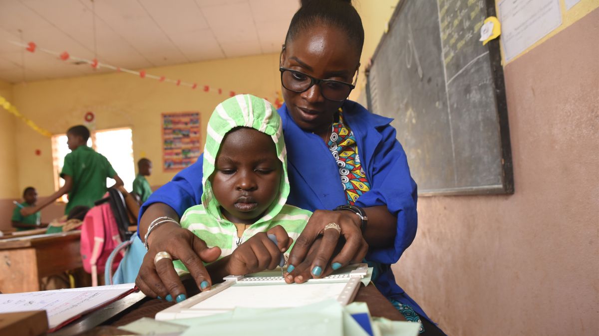 Lehrerin unterrichtet Kind mit Behinderung in der Schule in der Blinenschrift.<br/>