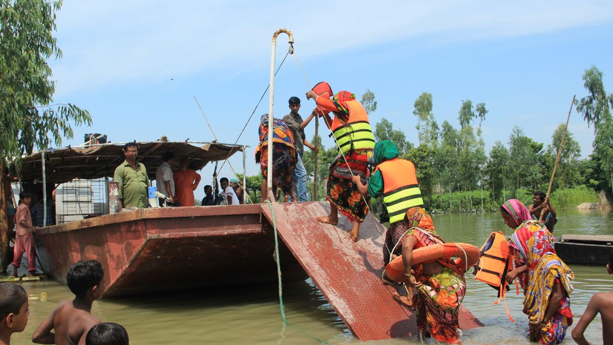 Mehre Menschen in Rettungswesten laufen aus dem Wasser über eine Rampe in ein Boot.