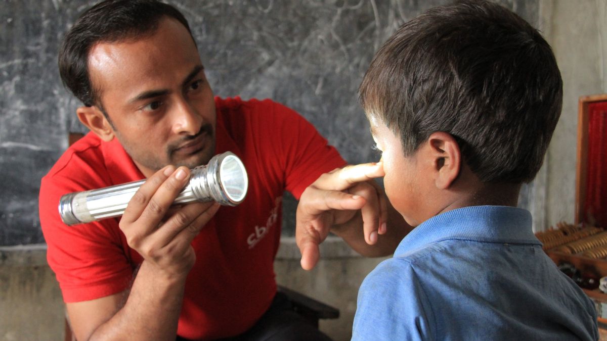 Ein Mann schaut mit einer Taschenlampe in das Auge eines kleinen Jungen.
