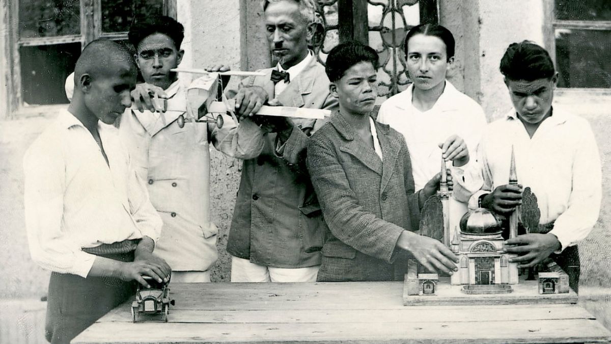 Ein älterer Mann ist umringt von mehreren Jungen, die Gegenstände befühlen.
