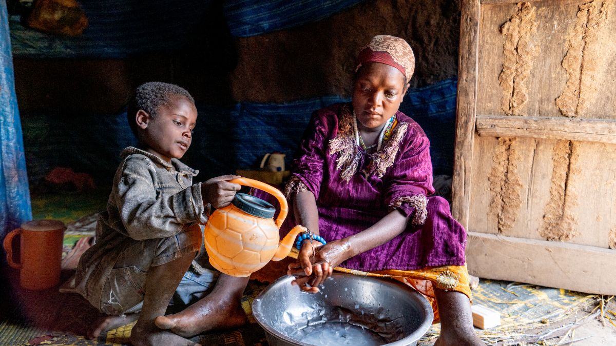 Ein kleiner Junge lässt Wasser aus einer Kanne über die Hände einer Frau laufen, damit sie sich waschen kann.