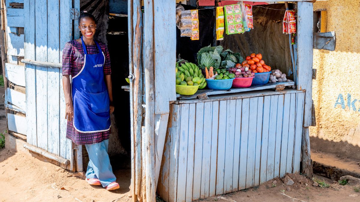 Eine junge Frau steht im Türrahmen ihres Marktstandes und lächelt in die Kamera.