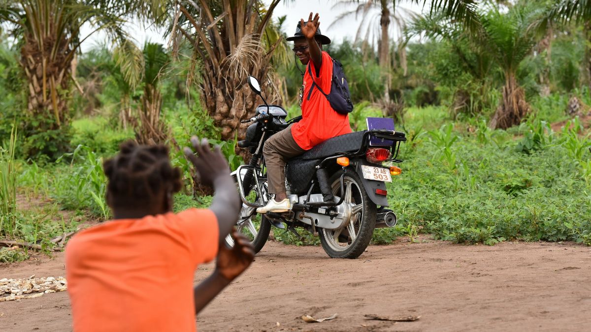 Eine sitzende Frau winkt einem winkenden Mann zu, der auf einem Motorrad sitzt.