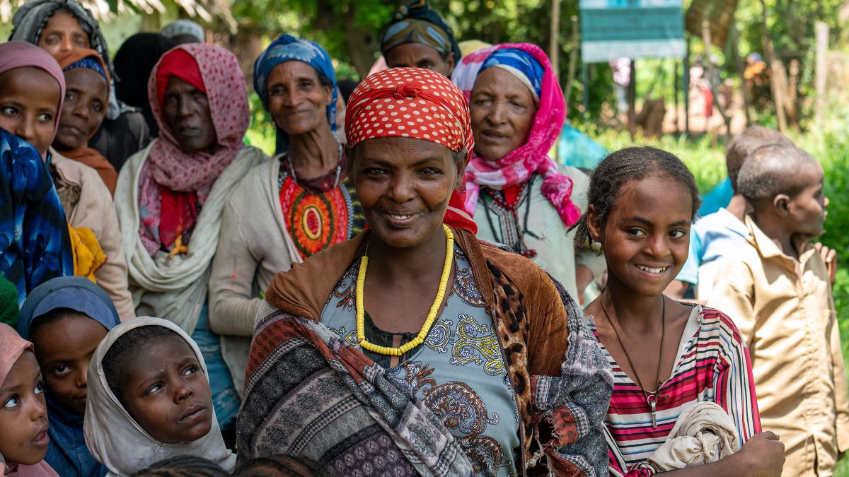 Eine lächelnde Frau ist umringt von Kindern und Erwachsenen.