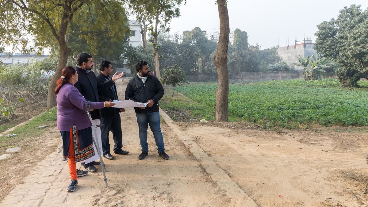 4 Personen stehen auf einen Weg und schauen gemeinsam auf einen Bauplan.
