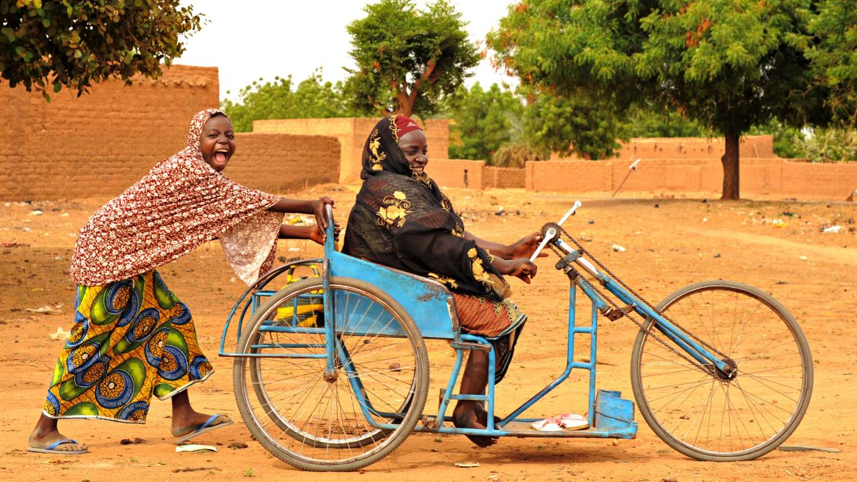 Lachendes afrikanische Frau schiebt eine andere Frau im Dreirad