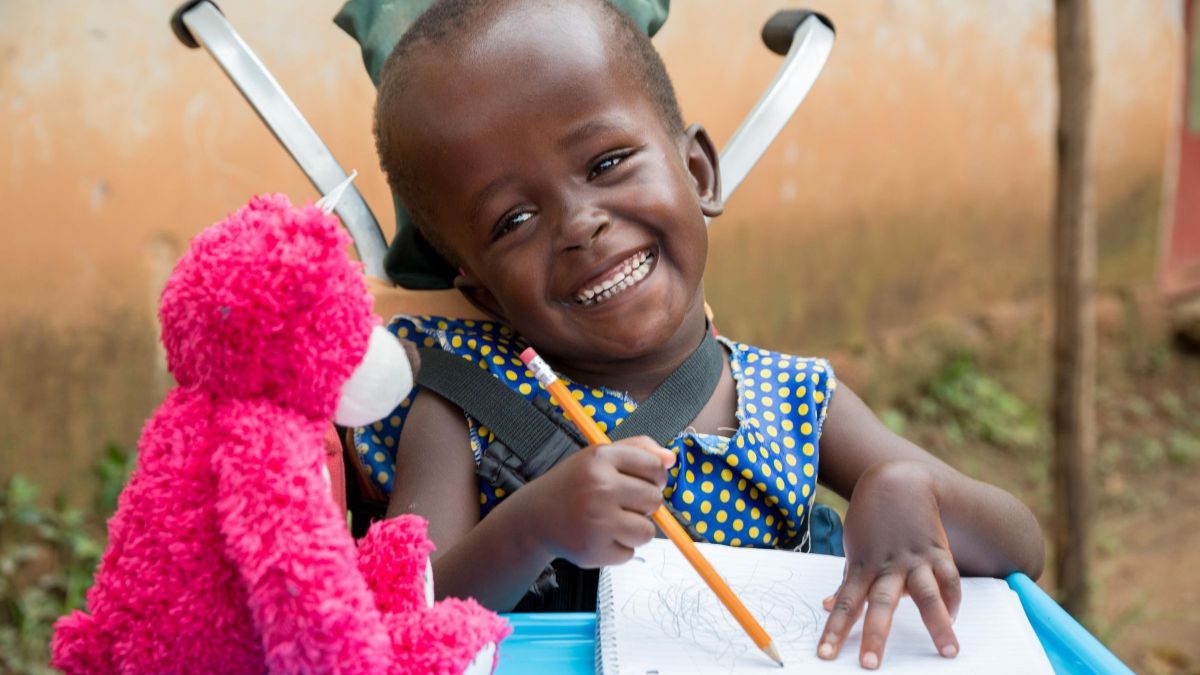 Die sechsjährige Justine aus Uganda wurde mit Hydrozephalus (&quot;Wasserkopf&quot;) geboren. Ein CBM-Gemeindehelfer fand die Sechsjährige: Jetzt bekommt sie regelmäßig Physiotherapie und macht tolle Fortschritte. Auf dem Bild freut sie sich über ein Geschenk - einen rosa Teddybären.