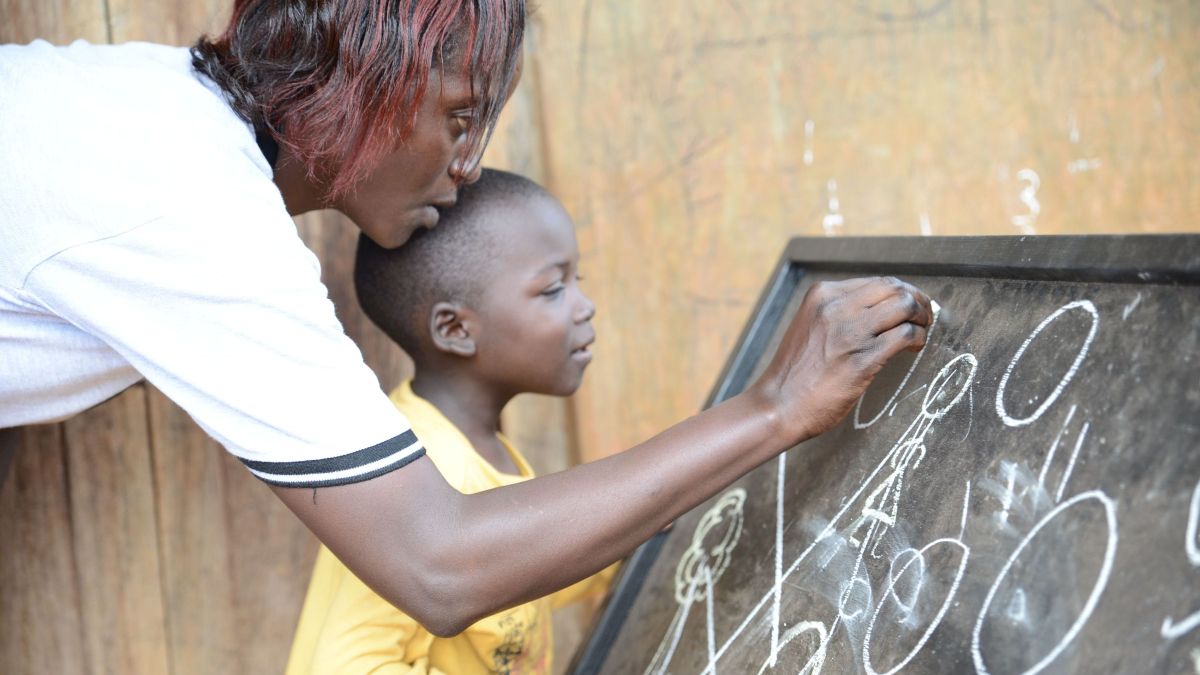 Eine Frau schreibt mit einem Kind zusammen mit Kreide auf eine Tafel