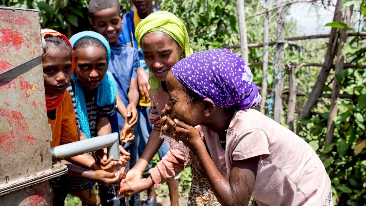 Afrikanische Schüler*innen waschen sich an einer Wasserpumpe das Gesicht