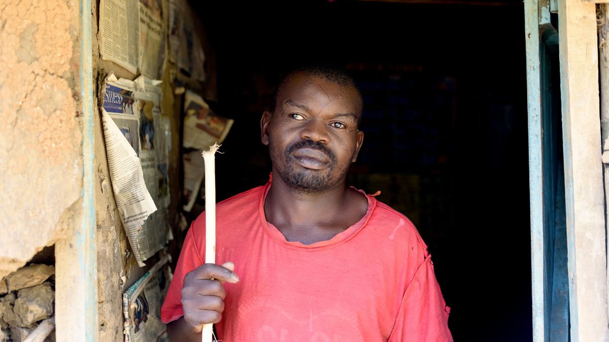Ein afrikanischer Mann mit Stock im Eingang einer Hütte, in der es dunkel ist.