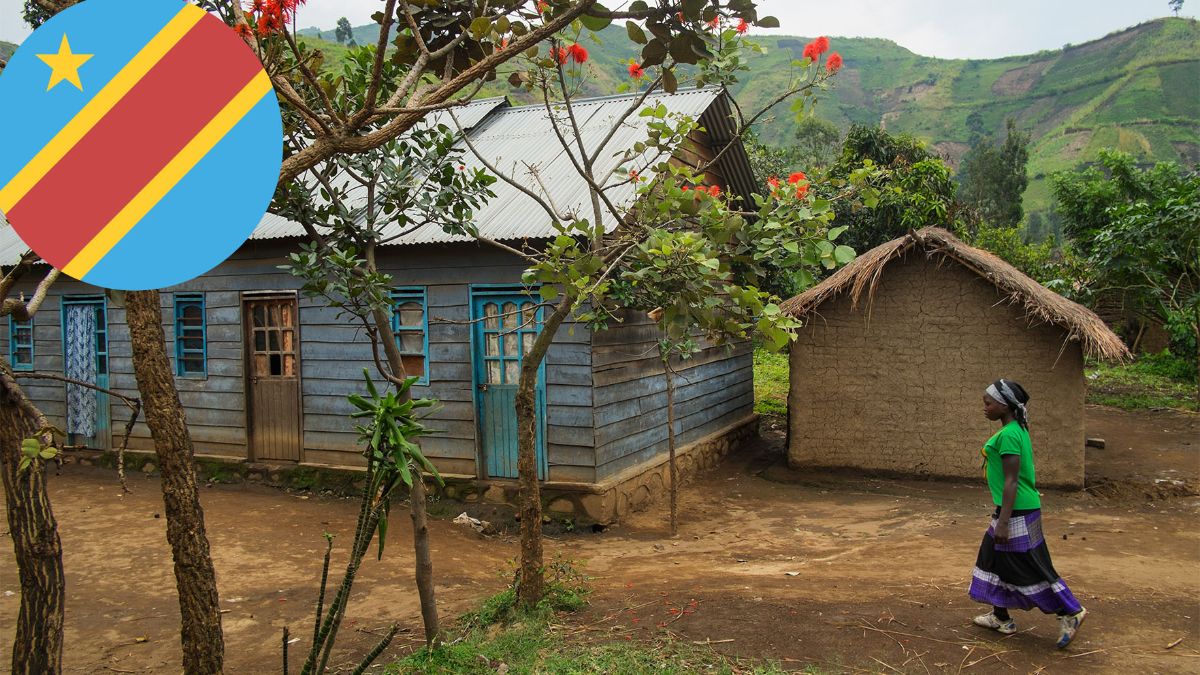 Ein Dorf in der Demokratischen Republik Kongo mit zwei Hütten und einer Frau im Vordergrund