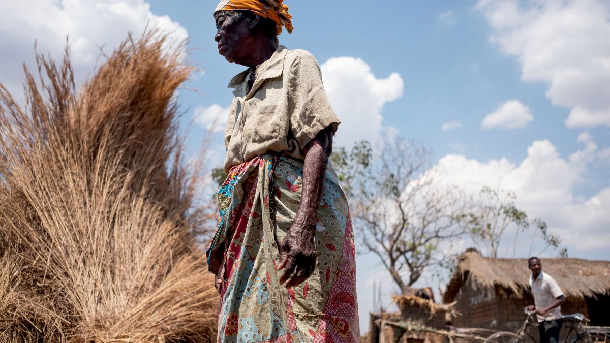 Eine alte Frau steht vor Bündeln von getrocknetem Gras