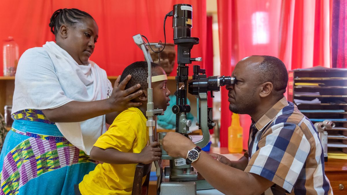 Ein Mann schaut durch ein Augenuntersuchungsgerät in die Augen eines Kindes.