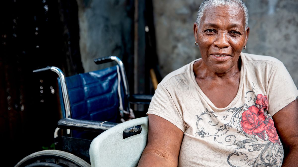 Ältere lachende Frau, im Hintergund: ein Rollstuhl.