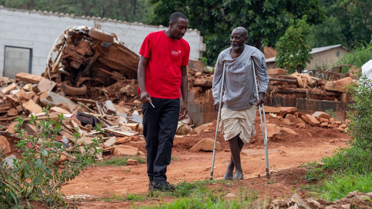 Zwei Männer gehen durch ein zertörtes Gebiet. Einer der Beiden läuft auf Krücken.