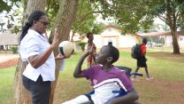 Eine Physiotherapeutin mit Ball in der Hand macht "High Five" mit Jungen im Rollstuhl