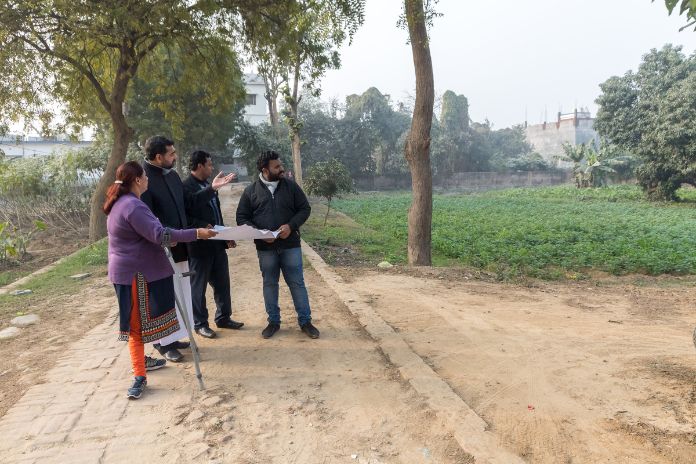 4 Personen stehen auf einen Weg und schauen gemeinsam auf einen Bauplan.