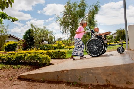Eine afrikanische Frau schiebt ein Kind im Rollstuhl eine Rampe hinauf.