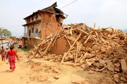 Menschen gehen an einem zusammengestürzten Haus vorbei. 