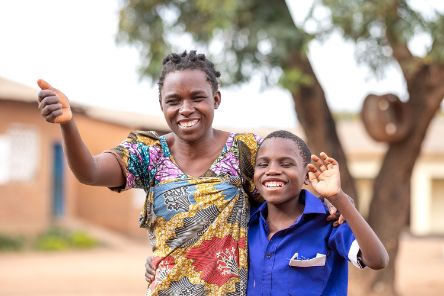 Eine Frau und ein Junge stehen eng beisammen, lachen und winken.