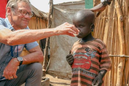 Ein Mann gibt einem Kind etwas aus einem Medikamentenbecher zu tringen.