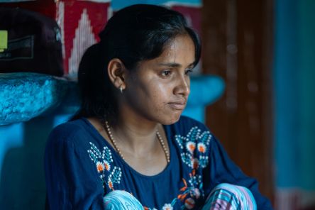 Ein Mädchen in blauer, bestickter Tunika, gestreifter Pluderhose und Pferdeschwanz sitzt an eine gemauerte Bank angelehnt.