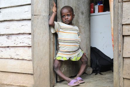 Ein etwa fünfjähriges Mädchen steht im Türrahmen einer Holzhütte.