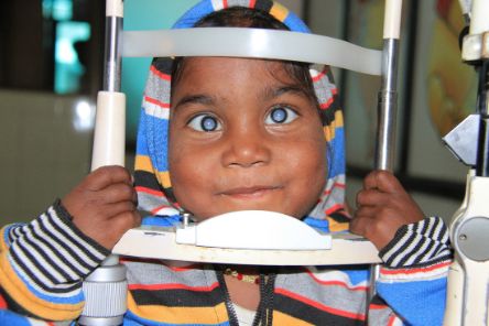 Ein Kind mit weißen Pupillen hat das Kinn auf ein Augenuntersuchungsgerät gelegt.