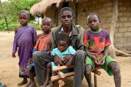 Ein Mann sitzt auf einer Bank. Neben ihn vier Kinder.