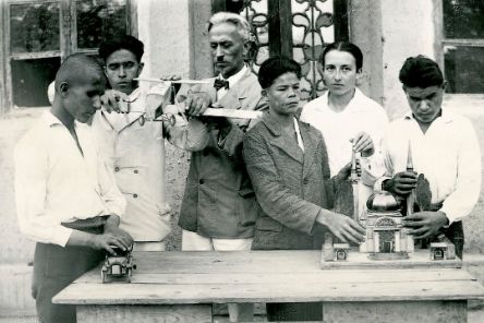 Ein älterer Mann ist umringt von mehreren Jungen, die Gegenstände befühlen.