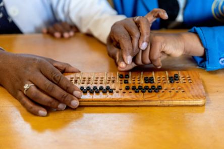 Eine Hand führt die Finger eines Kindes über eine Braille-Tafel.