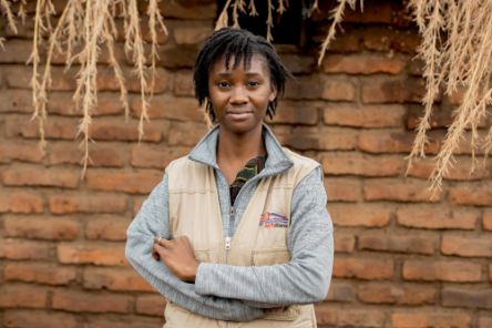 Eine junge Frau steht vor einer Wand aus Ziegeln und blickt in die Kamera.