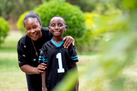 Eine Frau steht hinter einem Jungen und legt ihre Arme um ihn.