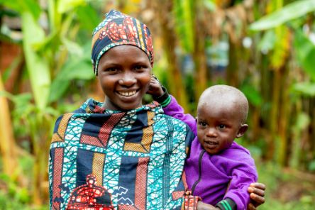 Eine junge Frau in bunter Kleidung und mit buntem Kopftuch trägt ein kleines Kind auf dem Arm.