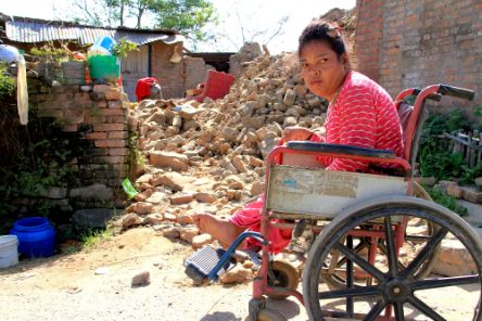 Eine Frau im Rollstuhl sitzt neben einem zerstörten Haus.