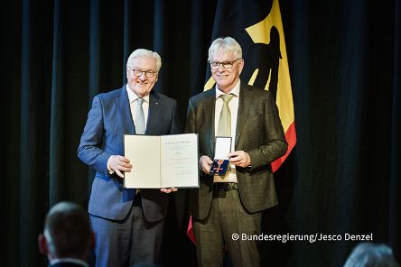 Zwei Männer stehen nebeneinander. Der eine hält eine Urkunde in den Händen, der andere ein Etui mit einer Medaille.