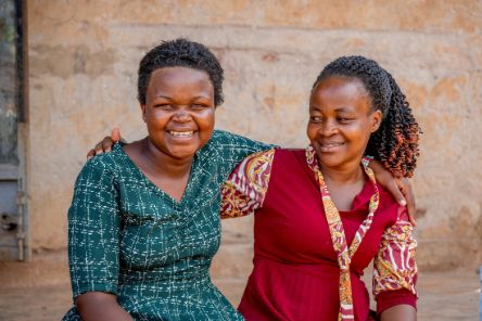 Zwei Frauen sitzen nebeneinander und haben jeweils einen Arm um die Andere gelegt.
