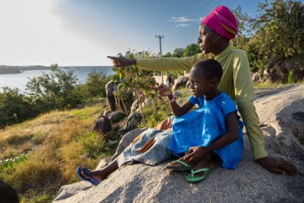 Eine Frau und ein kleines Mädchen sitzen auf einem Felsbrocken und schauen auf einen See.