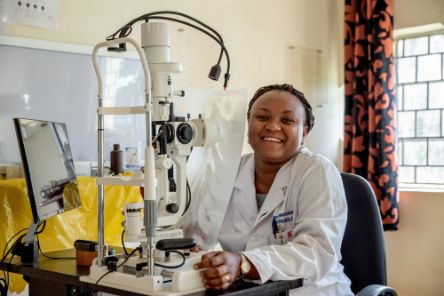 Afrikanische Frau im weißen Kittel sitzt an einem Apparat zur Untersuchung von Augen
