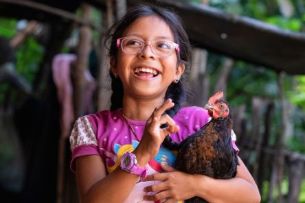 Ein Mädchen mit Zöpfen hält ein Huhn im Arm.