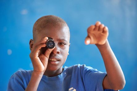 Arikanischer Junge hält eine Lupe vor sein rechtes Auge